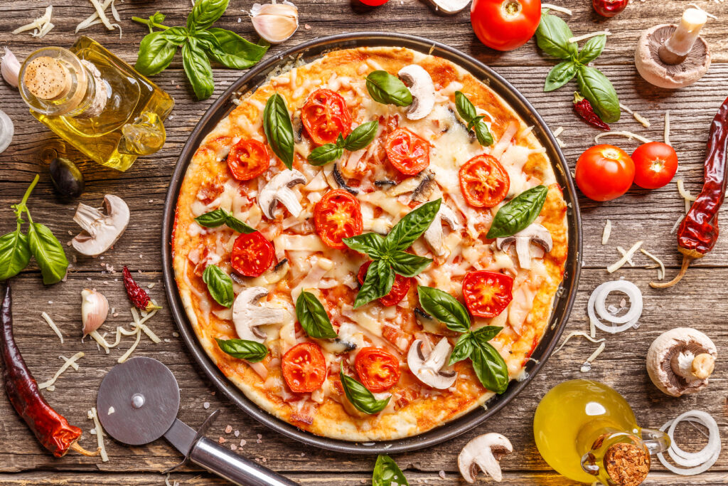 Picture of a pizza on a wooden board with various ingredients scattered around.